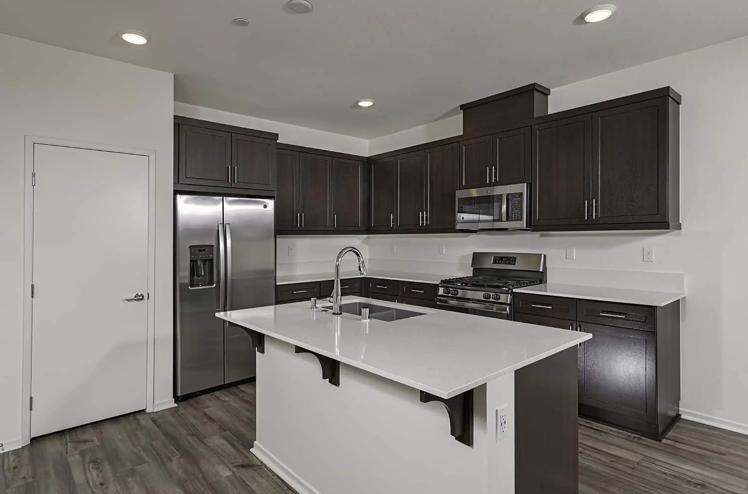 A kitchen with dark cabinets and white counters.