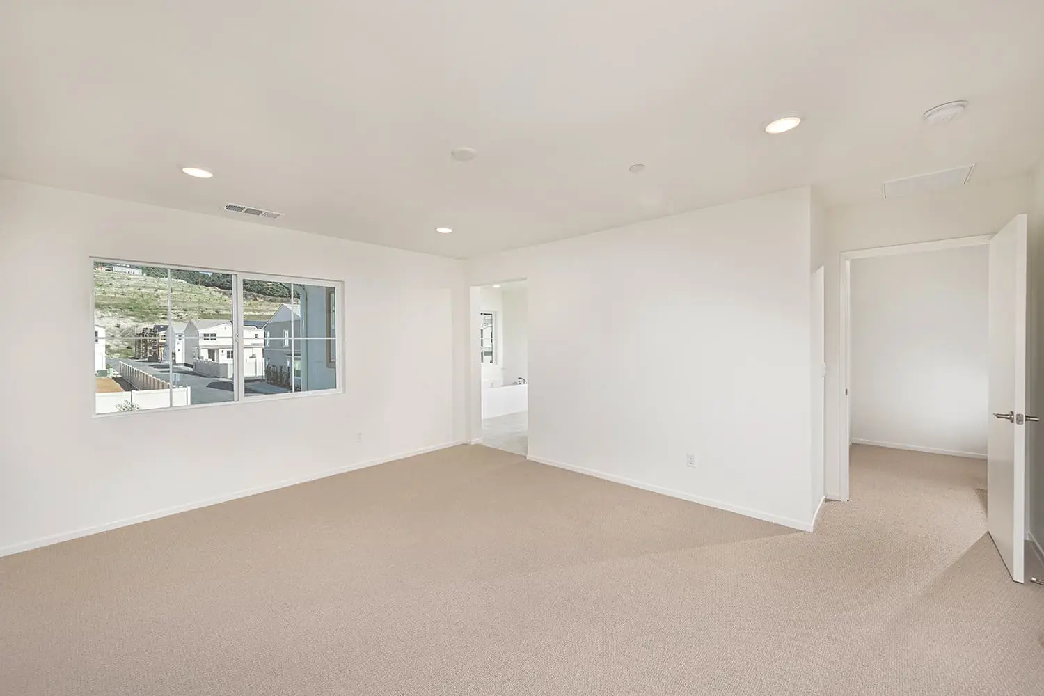 A large empty room with white walls and beige carpet.